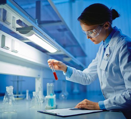 Woman views test tube at lab station.