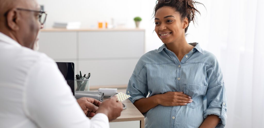 Doctor gives pills to smiling pregnant woman.