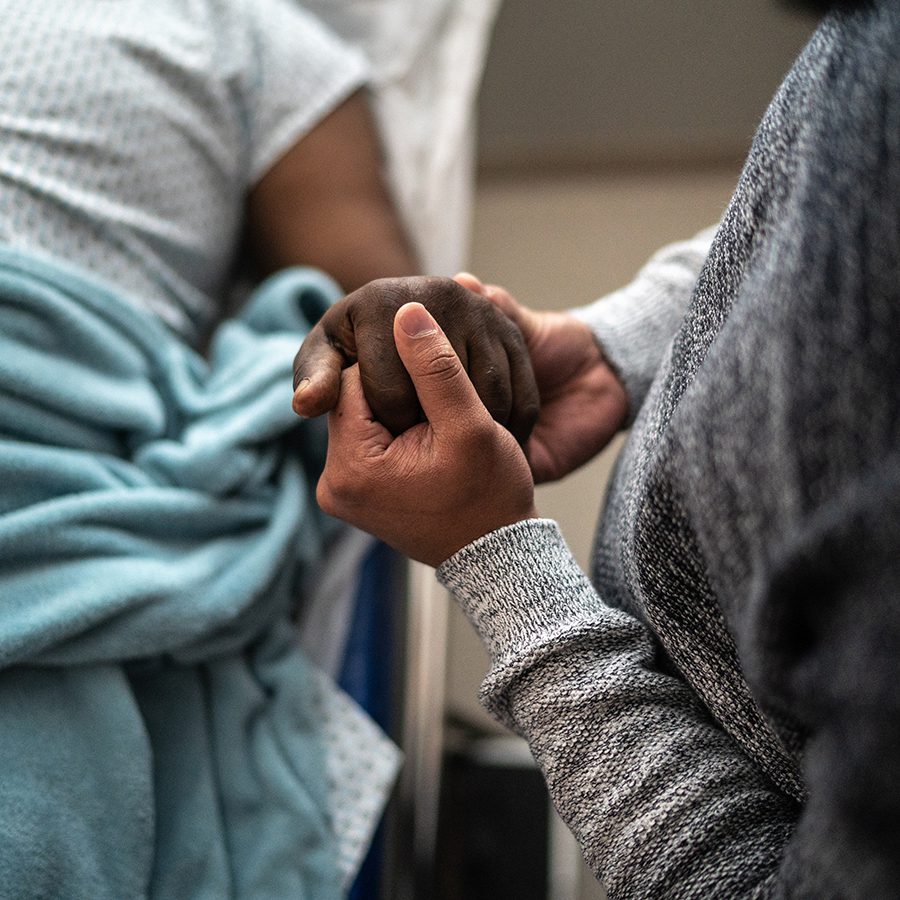 Son holding father's hand at the hospital, representing Black Directors Health Equity Agenda.