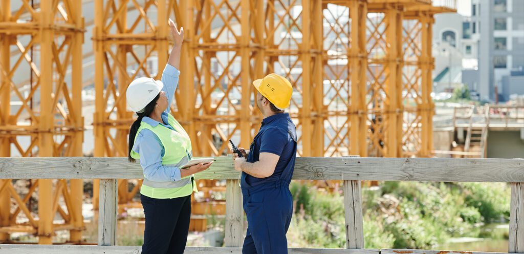 Woman and man in hard hats view building frame.