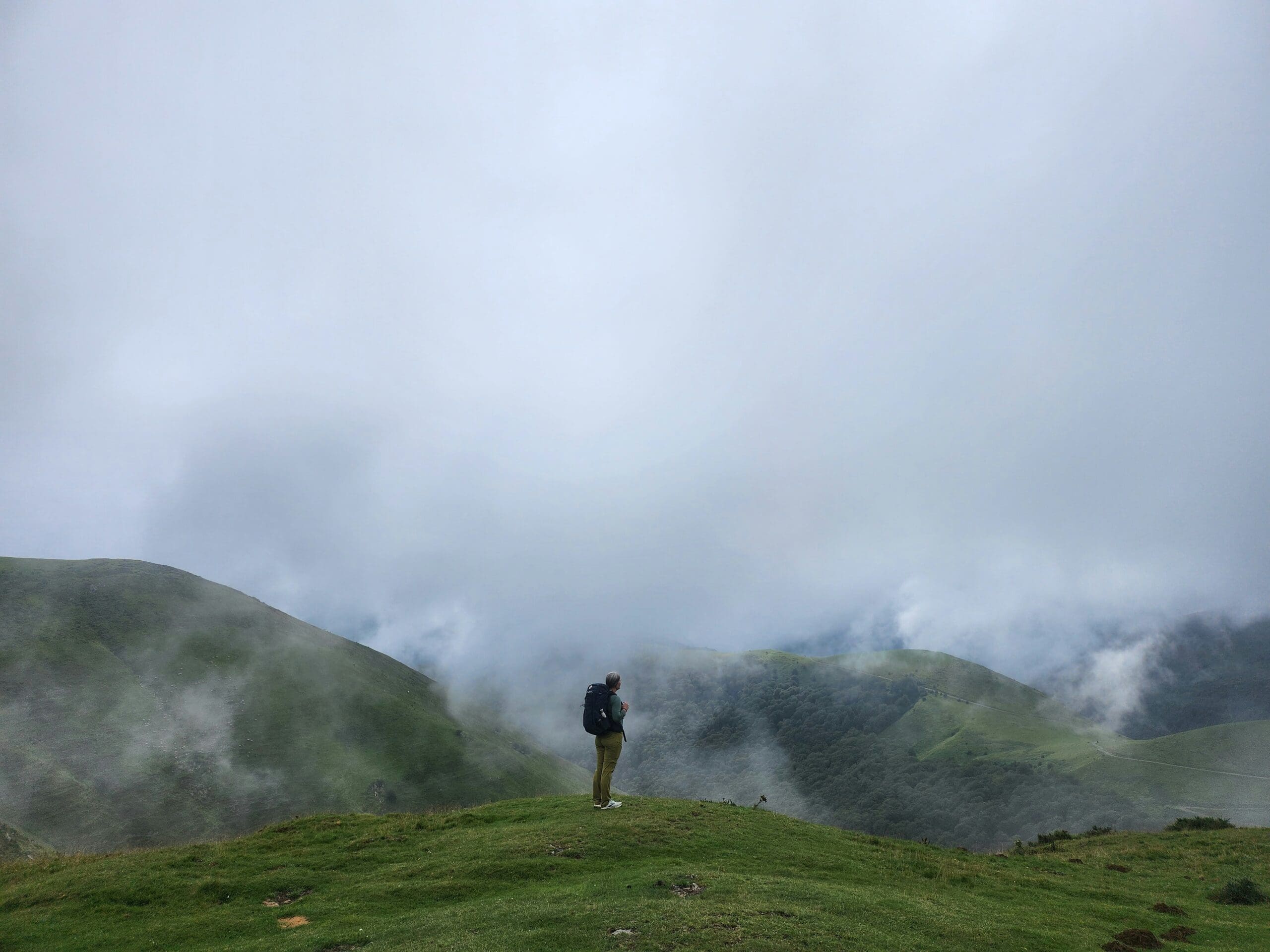 Man stands on green in misty, mountainous area.
