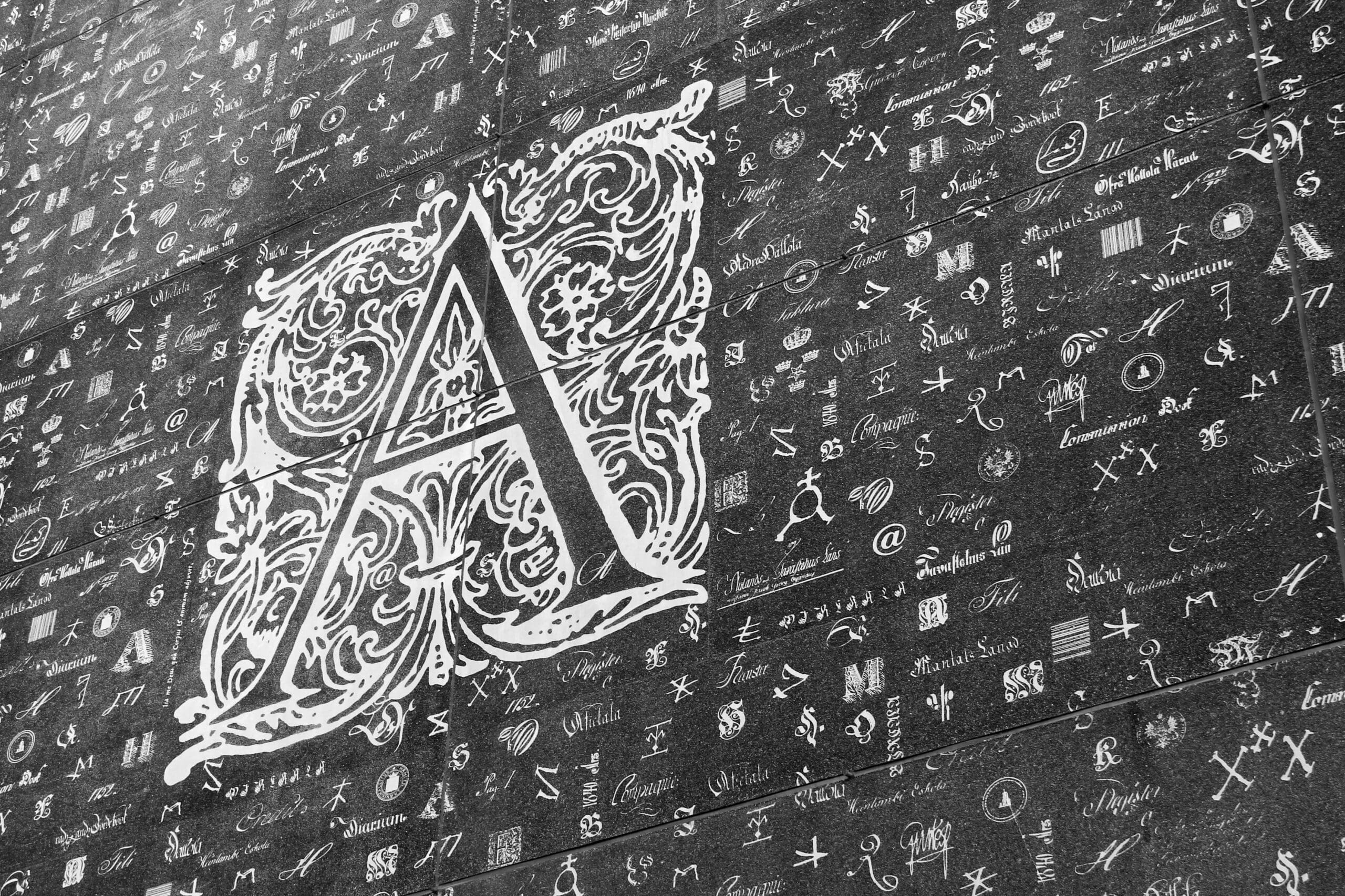 Alphabets, symbols and seals embedded in the facade of the National Archives of Finland.